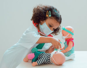 A little girl playing the doctor gives her patient an injection, they all wear protective masks